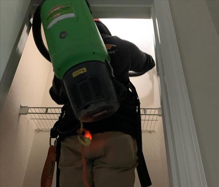 Man on a ladder looking into a closet with a HEPA vaccuum