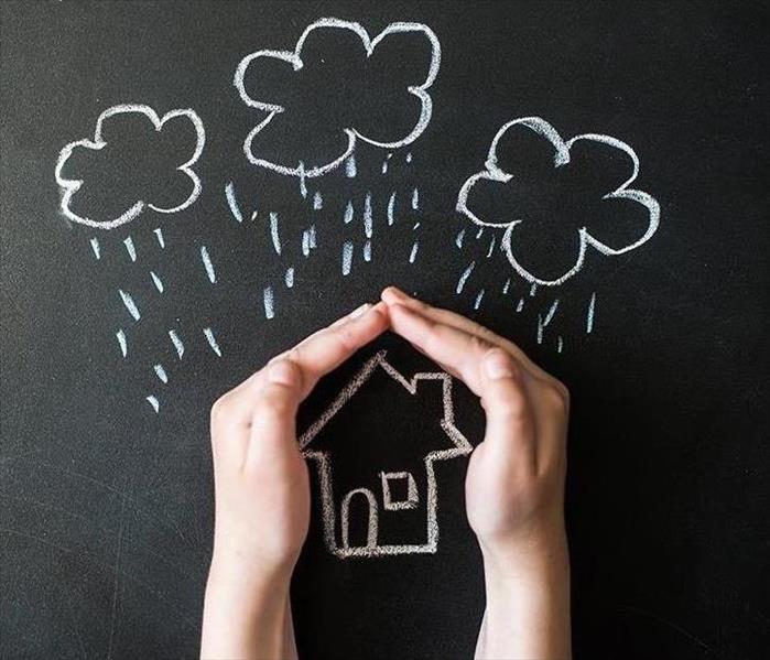 Hands covering a chalkboard drawing of a house with a storm overhead