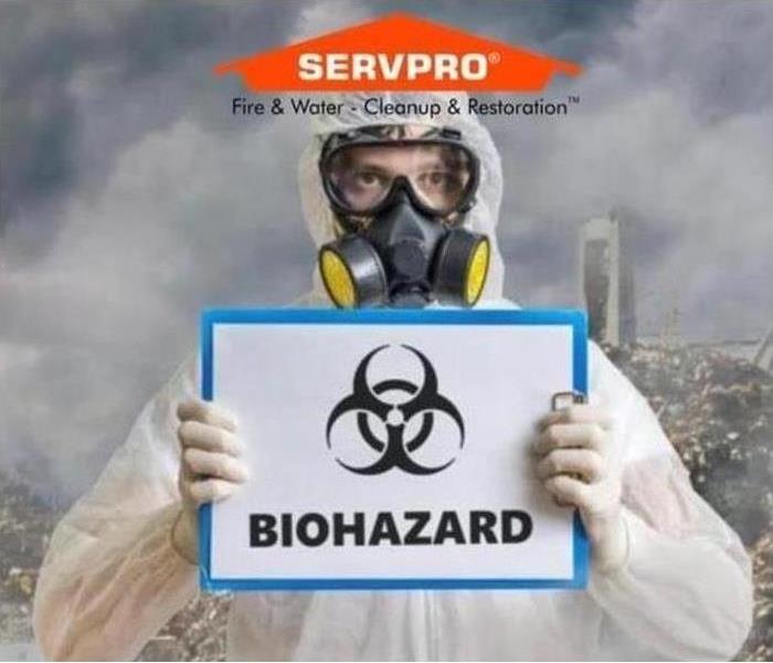 Man wearing PPE holding a sign that says "biohazard"